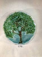 Front view of the round fused glass plate with Tree of Life design showing the green leafy canopy and brown metallic-glint tree trunk on a translucent background.