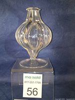 Front view of a clear hand blown glass vase with six lobes and a round base on a clear acrylic block.