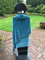 Turquoise shawl draped over mannequin from the back to show full size and color, set outdoors on a brick pathway with greenery background.