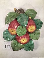 Full top-down view of the 3D ceramic wall plaque showing three red apples and surrounding green leaves glazed in majolica technique.