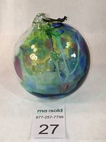 Front view showing multicolored swirling design of the glass orb with attached black hanging cord.