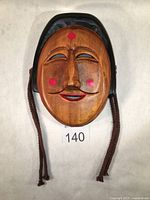 Front view of the wooden Korean traditional mask showing carved facial features, red painted dots, and braided cords.