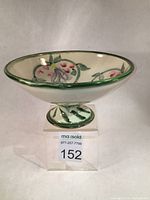 Front angled view of white stoneware compote dish with green rim, floral interior decoration and pedestal base.