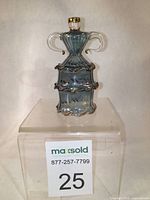 Front view of the light bluish-purple Murano glass perfume bottle with gold accents on clear acrylic stand showing tiered ruffles and two handle arms.