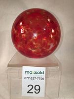Red confetti glass sphere photographed on transparent stand with visible lights reflecting off glass surface from various angles.