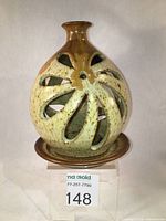 Front angled view of the ceramic tea light holder showing the floral pierced openings and glaze coloration on the globe along with the base plate beneath it.