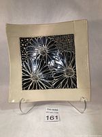 Top view of square white clay serving dish with carved black underglaze floral design and clear glaze