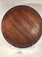 Top view of round black walnut wooden platter on clear stand, showing smooth dark wood grain surface.