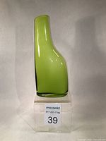 Side view showing the smooth, thick, lime green glass and asymmetrical shape of the vase on a clear stand.