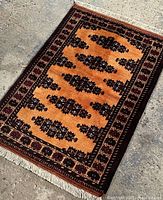 Full view of the handmade Persian Turkemen style rug showing the mustard yellow central field with black geometric motifs and dark borders with floral patterns.