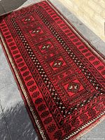 Full view of rectangular Baluch rug laid flat on ground showing central design and borders in natural light.