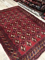 Full view of red hand-knotted wool rug laid out on floor with stacked rugs in background