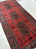 Angled full-length view of the red tribal rug showing three central panels and border patterns.