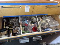 Opened drawer revealing multiple spools of gold-colored wire, plastic containers, and bags of assorted beads and jewelry making materials.