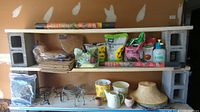 Shelving with gardening items including small pots, coco liners, garden sprayer, bags of soil amendments, palm fiber liners, and metal plant stands.