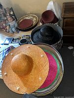 Photo of three woven wide-brim hats: orange with seashells, black with rhinestones, and a red hat, show color and decorative detail.