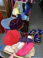 Full assortment of hats and scarves arranged on and in a chair and boxes showing variety of colors and materials.
