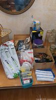 Shot from a distance of the full lot on a wooden table, showing multiple packages, small tool containers, jars, and hardware items in boxes.