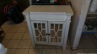 Front view of white painted wooden kitchen cabinet with mirrored doors showing molding and latticework detail on doors.