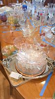 Shows overall assortment of pink depression glass serving dishes, metal trays, and colored glass goblets laid out on table