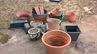 Wide view of all assorted planters showing variety of sizes and materials, placed on outdoor ground with visible dirt and weathering