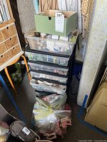 Full stack of plastic drawers loaded with thread spools, clear tote on top, cardboard box above and large zip bag at base