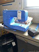 Blue New Home Janome sewing machine model 311LE with foot pedal on table near window.