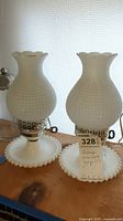 Pair of vintage milk glass lamps shown with hobnail textured shades and scalloped edge round bases, with handwritten tag indicating they are milk glass lamps.