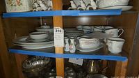 Full display of the china pieces arranged on wood shelves, showing cups, saucers, platters, serving bowls and other items visible with floral pattern and silver trim