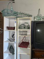 Photo of white shelving units holding several wire and metal baskets including blue planter basket with heart decoration, red heart basket, and green wire baskets.