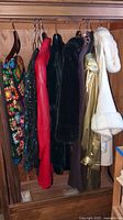 Six women's coats of various styles and colors hanging in a wooden wardrobe.