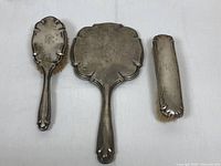 Three-piece 800 silver vanity set including hand mirror, hair brush, and lint brush photographed from the front on a white background.