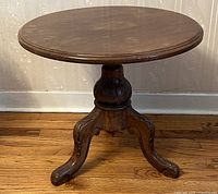 Full view of the round wooden pedestal table showing top, carved pedestal, and legs.