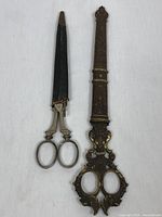 Pair of antique scissors: one large with ornate brass handle and sheath, one smaller with black sheath showing wear