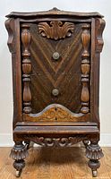 Front view showing wood grain, ornate carvings on sides and drawers, two drawers with metal knobs, supported by carved feet with metal casters.
