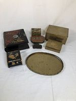 Full view of lot showing all brass and lacquered boxes and oval brass tray on white background.