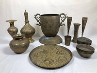 Full lot of brass items arranged on flat surface including vase on stand, platter, goblets, and small bowls