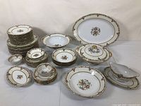 Full lot overview showing stacked plates, bowls, covered casseroles, gravy boat with saucer, and platters all displaying consistent floral pattern with gold trim.