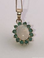 Front view of pendant showing oval opal and emerald halo