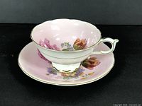 Side angle of the teacup on the saucer showing the pink floral design and gold trim.