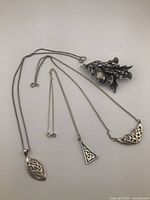 Three silver Celtic pendants on chains and silver-toned bagpipe brooch with thistles.