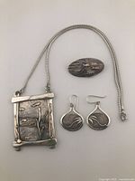 Front view of the fish-themed pendant, earrings, and brooch laid out showing design details and chain.