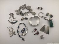 Photo showing multiple sterling silver jewelry pieces including charm bracelet, various earrings, and pendants.