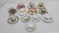 View of all eleven teacups and saucers arranged on a white surface showing various designs and colors