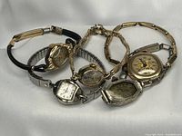 Five gold-tone ladies wristwatches arranged on white background