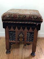 Front view of stool showing upholstered top and carved wooden base