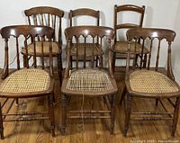 Set of four vintage wooden chairs with cane seats shown from front, including one with wooden arms and three armless chairs. One cane seat shows damage.