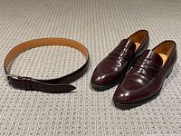 Full view of oxblood leather loafers and matching belt laid out on carpeted floor.