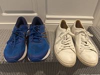 Photo showing front view of ASICS blue running sneakers and SuitSupply white leather sneakers placed side by side on carpeted floor.