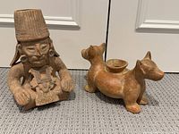 Photo showing pair of Mexican terracotta pottery vases on carpeted floor in front of white doors, one a seated human figure and the other animal-shaped.